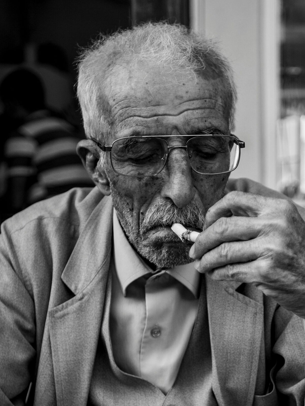 Älterer Mann mit Brille und grauem Haar raucht eine Zigarette, trägt Anzug und Hemd