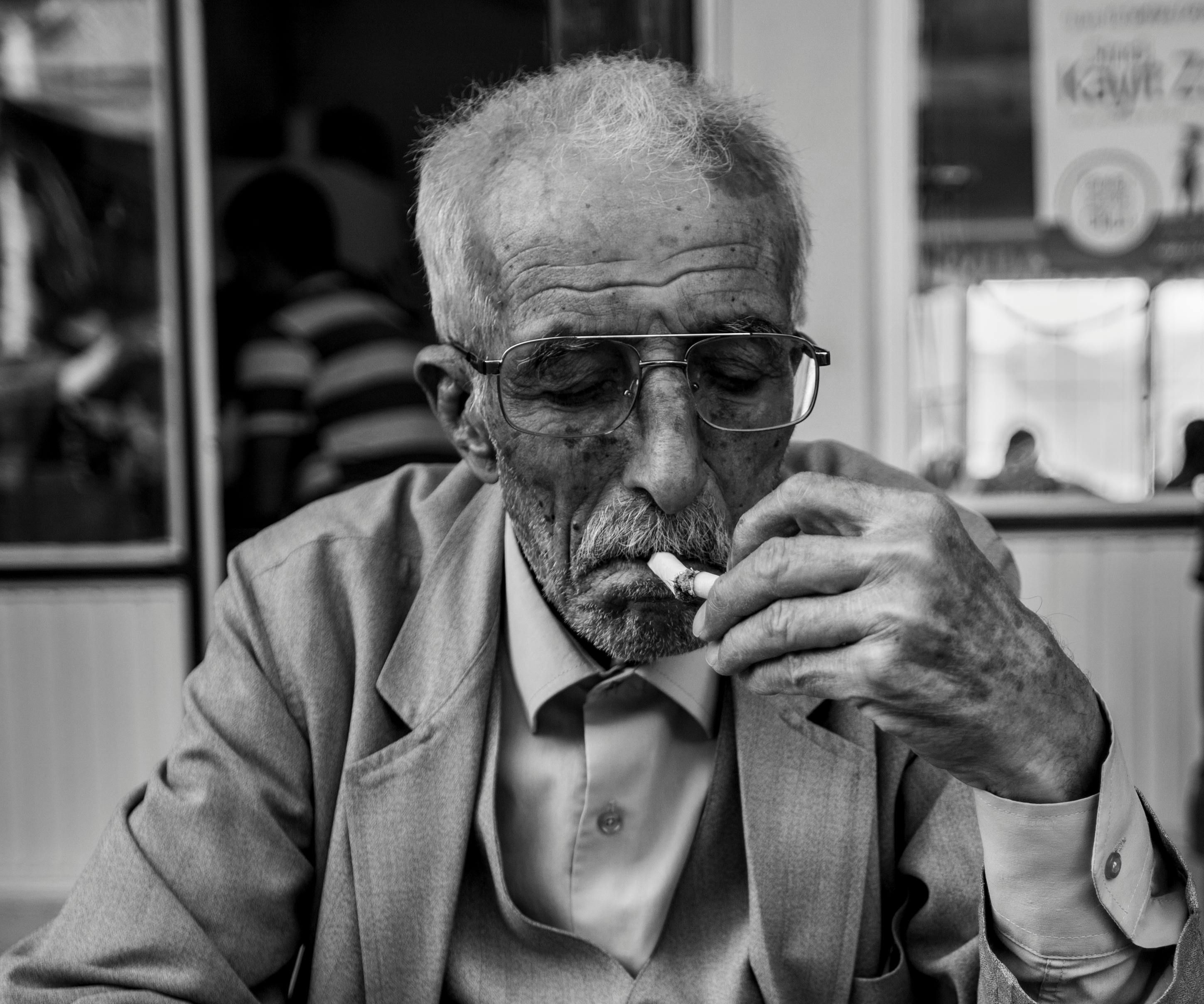 Älterer Mann mit Brille und grauem Haar raucht eine Zigarette, trägt Anzug und Hemd