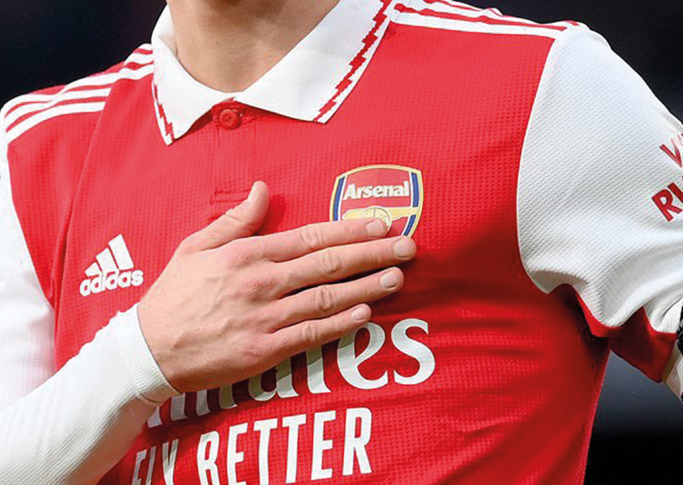 Hand auf dem Arsenal-Fußballtrikot mit rotem Oberteil und weißem Kragen und Ärmeln, Adidas-Logo und Schriftzug 'Emirates Fly Better' sichtbar