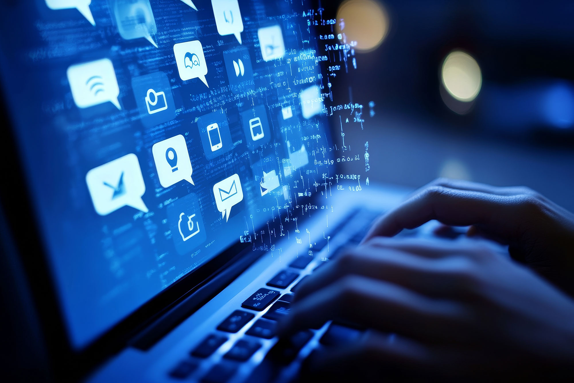 Hände tippen auf Laptop-Tastatur mit schwebenden digitalen Symbolen für Kommunikation und soziale Medien